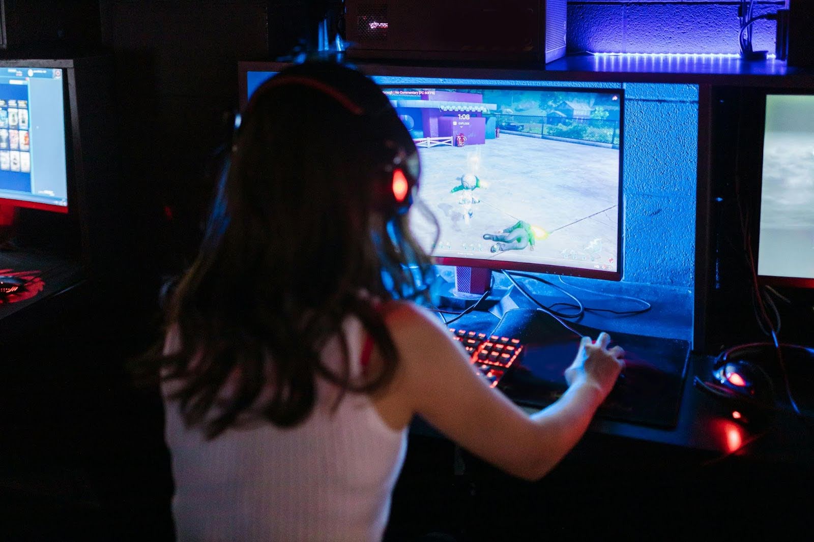 ゲーミングヘッドセットを着けた女性が、明るいキーボードとマウスでPCゲームをプレイしている様子。