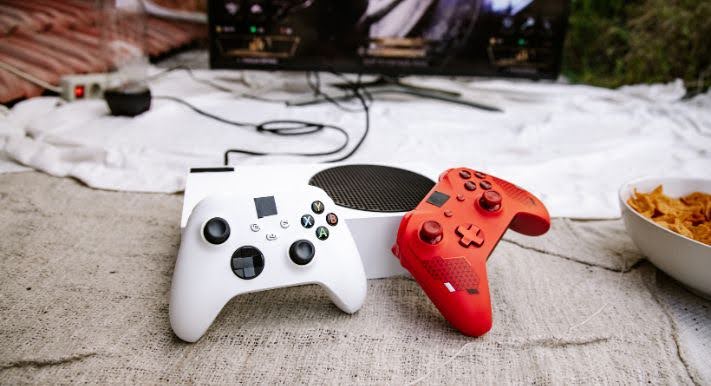 白と赤のXboxコントローラーと本体、横にスナック菓子のボウル