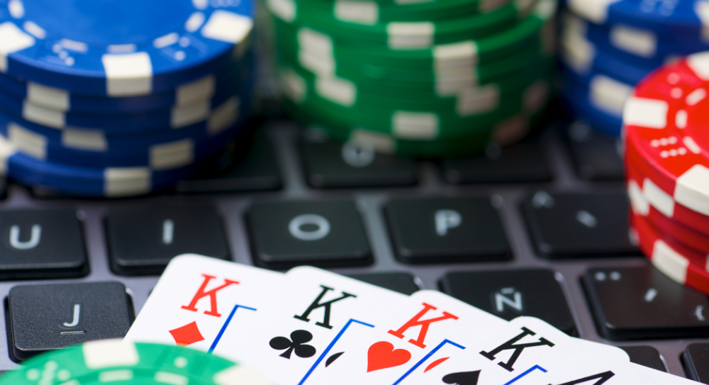 ノートパソコンのキーボードの上に、トランプの4枚のキング（全スート）と、青・緑・赤のカジノチップが重ねて置かれている画像。